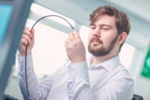 Man with beard inspecting long cable in brightly lit room