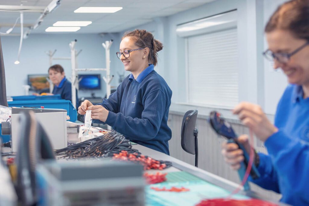 Two women sat at a workstation inspecting and assembling cable
