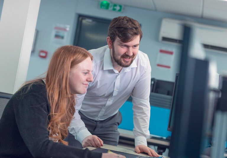 A man and a women working at a workstation, looking at a computer screen