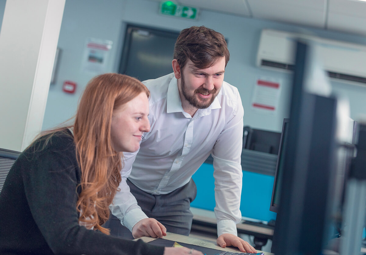 A man and a women working at a workstation, looking at a computer screen